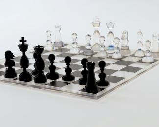 a glass chess board with black pieces on it by Alexander Mils courtesy of Unsplash.